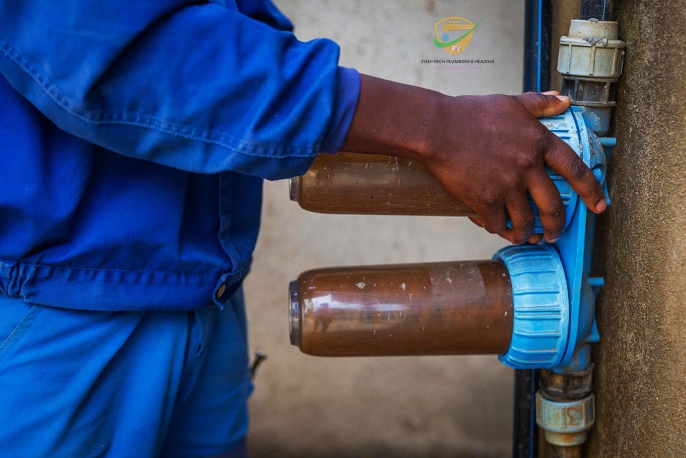 A certified plumber from Foli-Tech performing professional plumbing services in Ghana — fixing a leaking pipe under a kitchen sink.